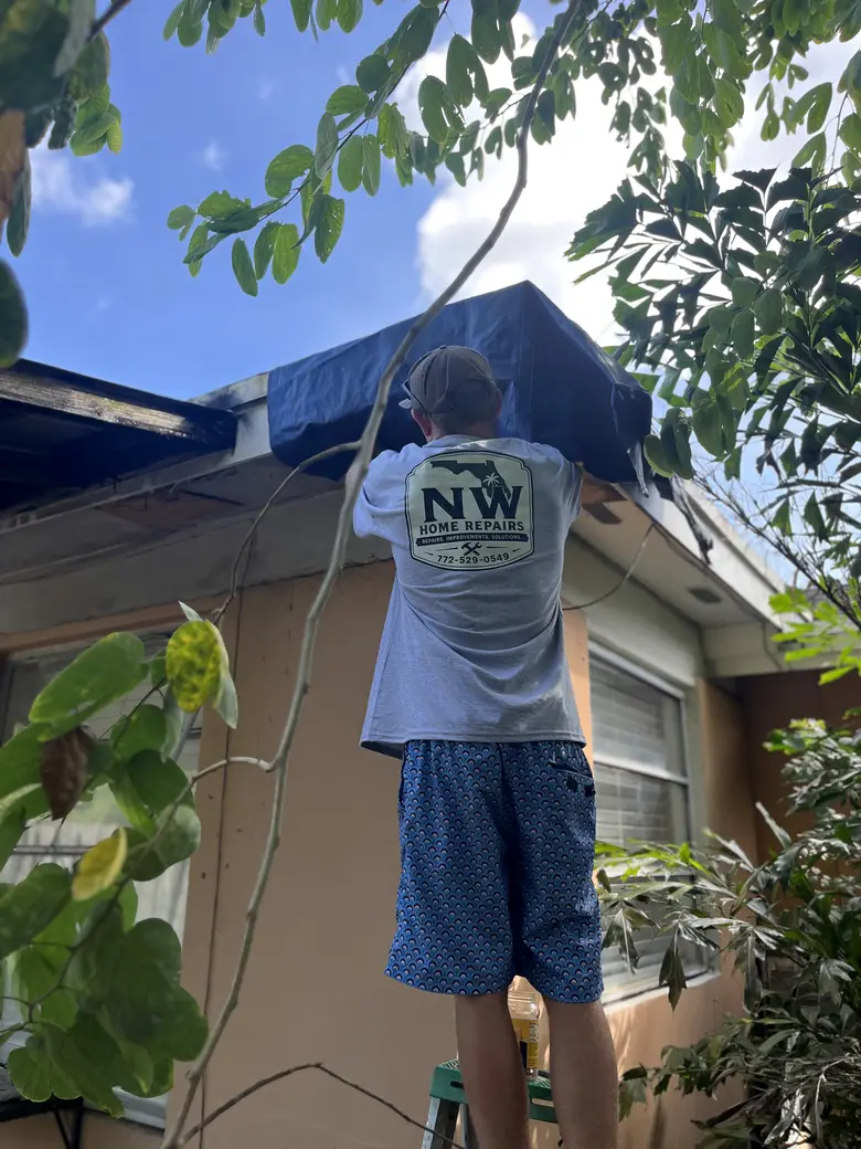 Nick on a ladder in his NW Home Repairs shirt, fitting the tarp over the damage